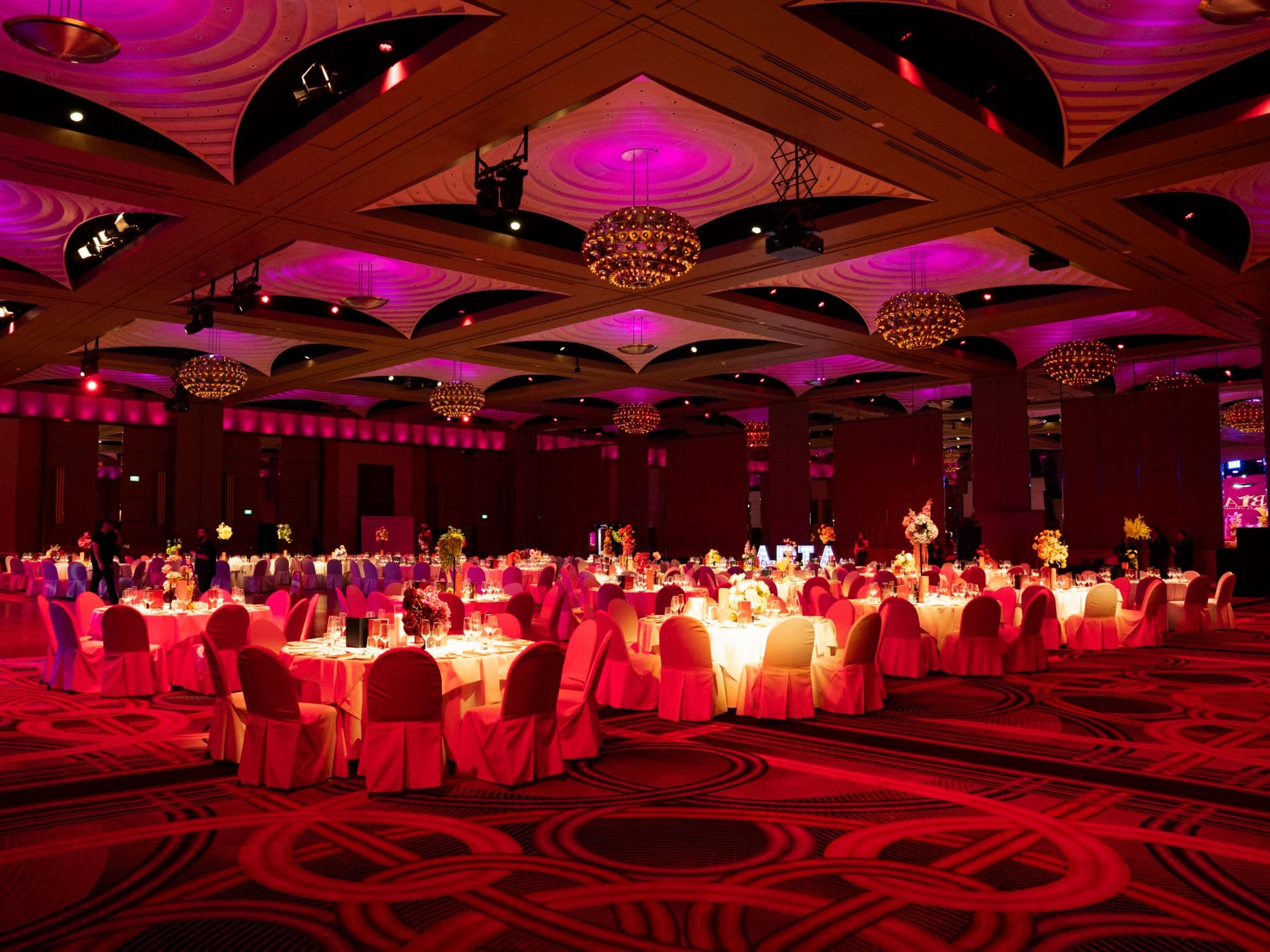 Gala ballroom with chandeliers and dressed tables under magenta light