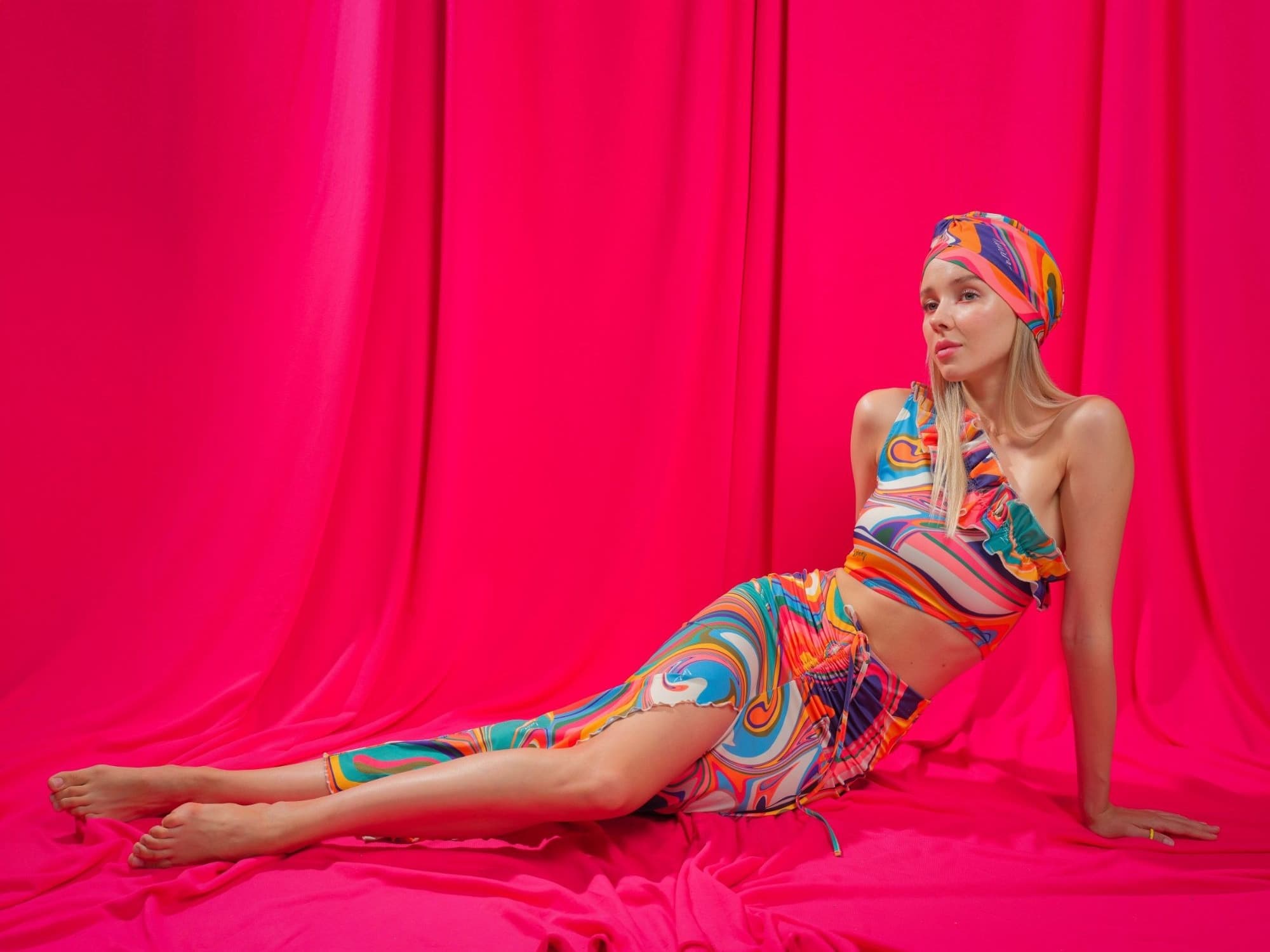 Model in a swirl-print turban, top and skirt reclining on a pink backdrop